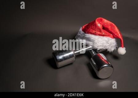 Dumbbells fitness red santa claus hat on black background Stock Photo