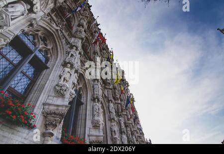 Leuven, Belgium, August 2019. View of the facade of the town hall richly decorated with statues and colored flags. Stock Photo