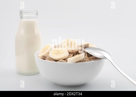 Healthy breakfast and rich  source of calcium and fiber concept with generic shredded wheat cereal and banana slices, bottle of milk and spoon isolate Stock Photo
