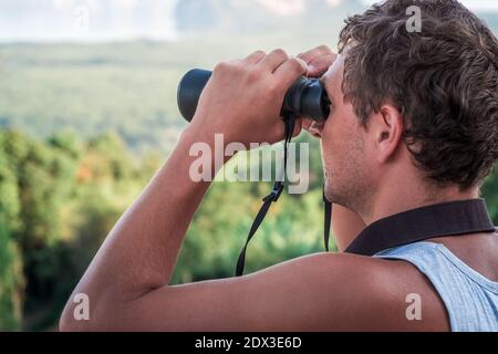 A young man looks into the distance through binoculars. Stock Photo