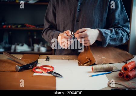 An experienced tanner sews a clasp for a leather product with stitches. Stock Photo