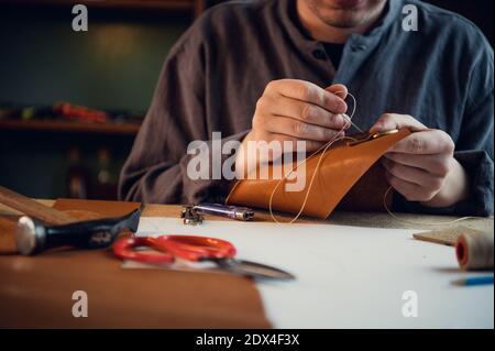 A young shoemaker manually sews decorative elements to leather shoes in the workshop. Stock Photo