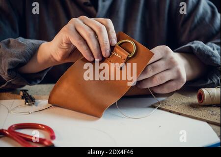 A young shoemaker manually sews decorative elements to leather shoes in the workshop. Stock Photo