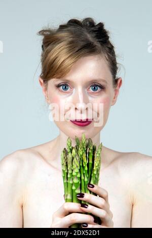 Beautiful young woman holding asparagus in her hands showing eating healthy food Stock Photo