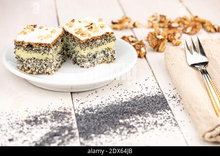 Poppy cake with creamy filling and walnuts on the top of dessert. Served on white wooden retro table and golden form in warm colors. Homemade dessert. Stock Photo