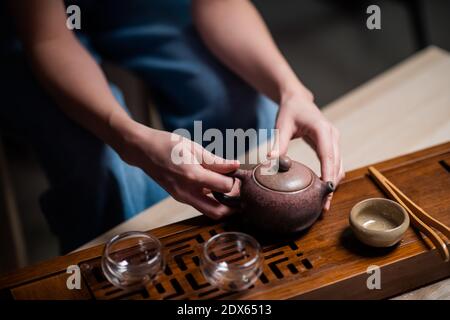 The girl is holding a ceramic teapot. Close-up of a table for a ritual tea party in China. Bamboo table with tray and cups Stock Photo