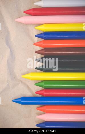 A set of lined up colored wax crayons on recycled paper background ...