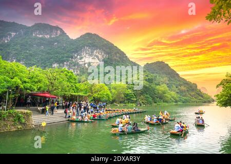 Ferry man rowing boats carrying tourists on river of the Tam Coc National Parkin sunset sky. This is a popular tourist destination Stock Photo
