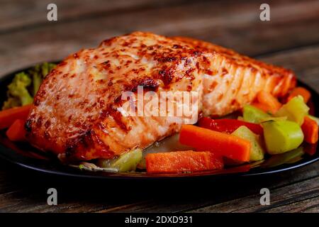 Baked juicy salmon fillet with steamed vegetables on black plate. Healthy food. Stock Photo