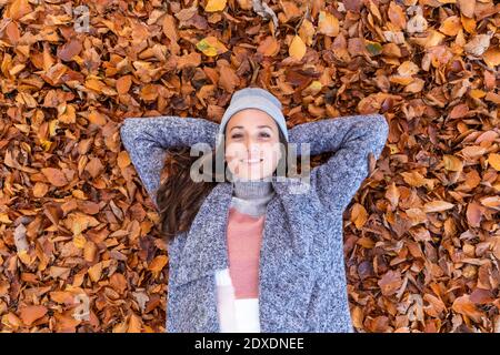 Smiling female hiker with hands behind head lying down on autumn leaves in Cannock Chase woodland Stock Photo