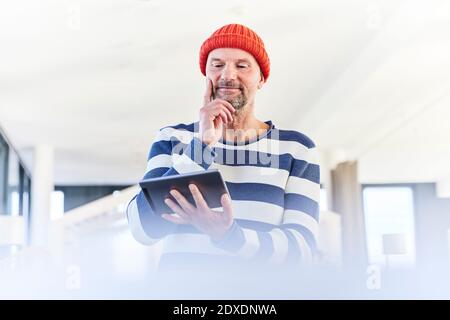 Thoughtful man using digital tablet while standing at home Stock Photo