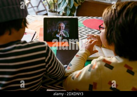 Boys on video call with teacher while e-learning through digital tablet at home Stock Photo