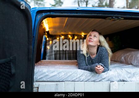 Thoughtful woman looking up while lying on bed in motor home Stock Photo