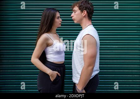Couple looking at each other while standing with hands in pockets against shutter Stock Photo