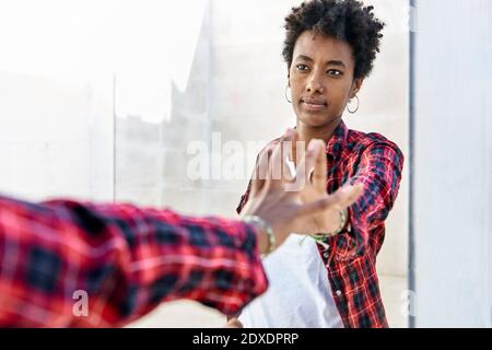 Young Afro woman with serious expression touching her mirror reflection Stock Photo
