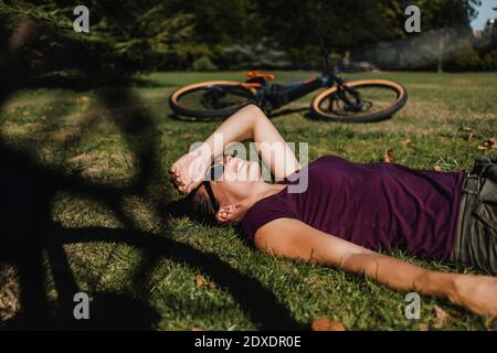 Woman lying on grass while resting by mountain bike at park Stock Photo