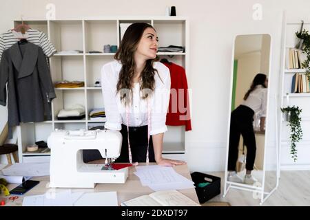 Female fashion designer looking away while leaning on desk in studio Stock Photo