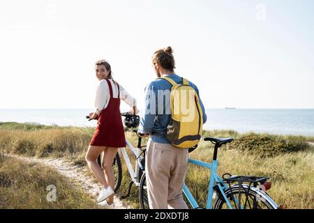 Young man and woman with bicycles walking on footpath against clear sky Stock Photo