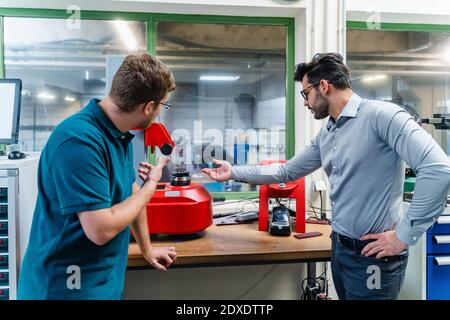 Businessman and male colleague discussing about surveyor machine while standing in industry Stock Photo