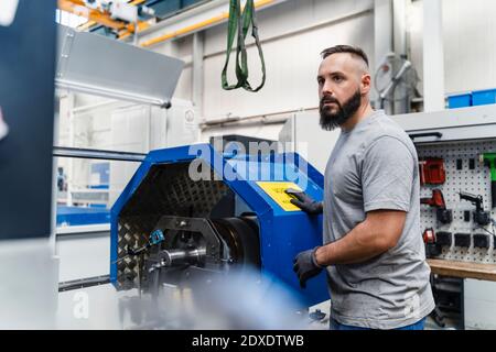 Thoughtful male technician looking away while standing by machine in factory Stock Photo