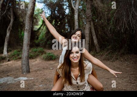 Mother giving piggyback ride to daughter in forest Stock Photo