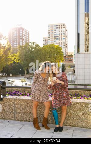 Young woman with prosthetic leg using smart phone by female friend