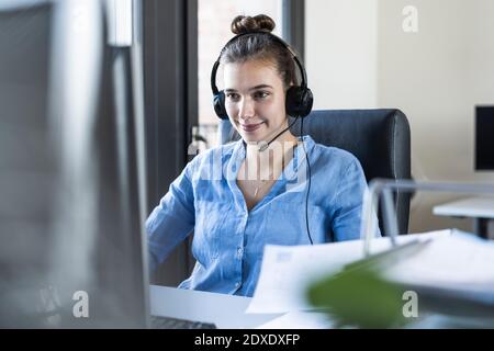 Young businesswoman wearing headphones working on computer while sitting at office Stock Photo