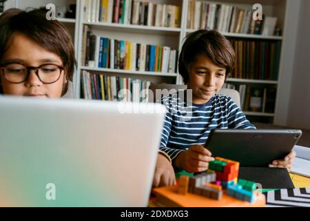 Smiling boy using digital tablet sitting with male friend at home Stock Photo