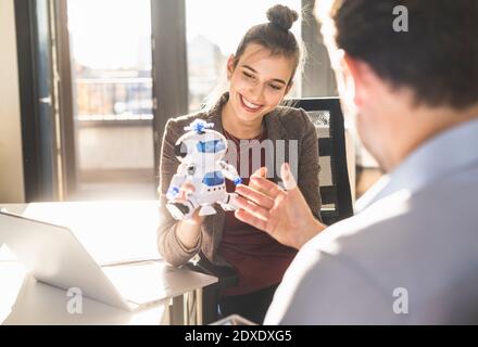 Young businesswoman showing robot toy to businessman while sitting at office Stock Photo