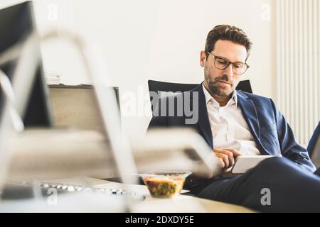 Businessman using mobile phone while having lunch sitting at office Stock Photo