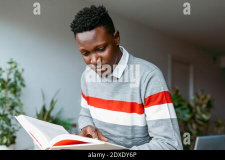 Male freelancer doing research while reading book at home Stock Photo