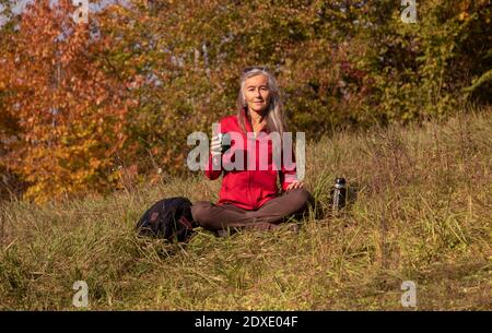 Woman holding thermos cup while sitting on mountain at Alpine Foothills, Germany Stock Photo