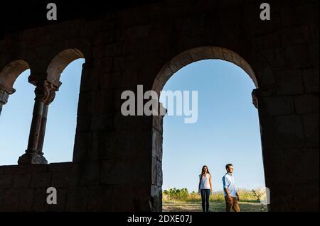 Young couple standing on field seen through arch at Roman church Stock Photo