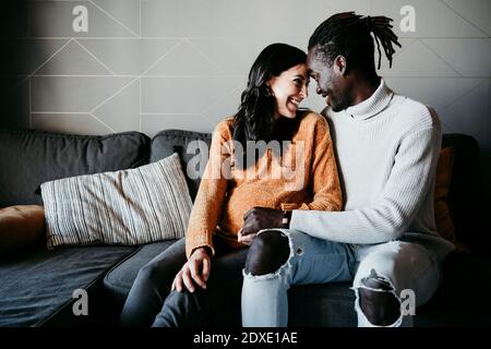 Romantic man with pregnant woman looking at each other while sitting on sofa at home Stock Photo