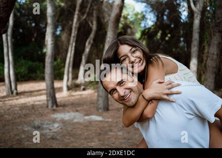 Happy father giving piggyback to daughter in forest Stock Photo