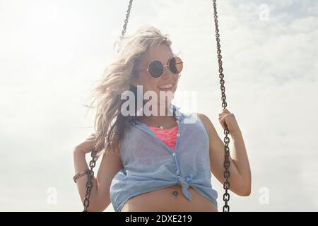 Happy young woman on swing against sky on sunny day Stock Photo