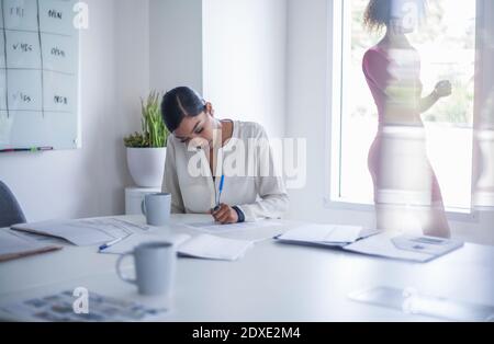 Young businesswoman writing on paper at desk while sitting in office Stock Photo