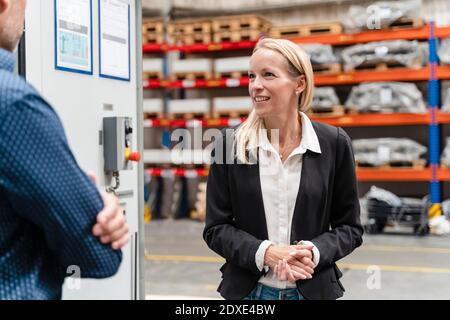 Smiling businesswoman with hands clasped discussing with male colleague in factory Stock Photo