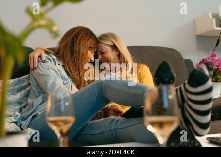Smiling mother and daughter with arm around touching foreheads on sofa Stock Photo