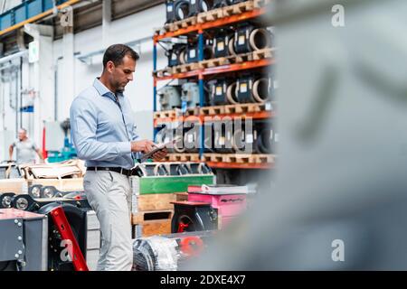 Male entrepreneur concentrating while using digital tablet standing at industry Stock Photo