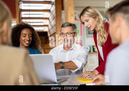 Businessman using laptop while explaining colleagues in meeting at office Stock Photo