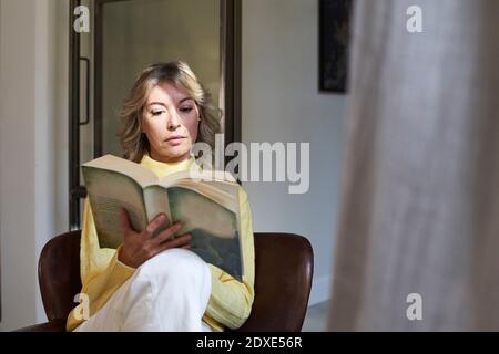 Mature woman in yellow sweater reading book at home Stock Photo