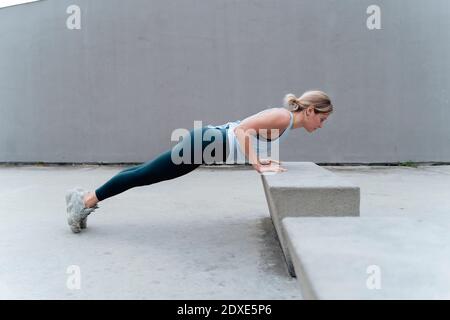 Sportswoman doing push-ups while exercising against wall Stock Photo