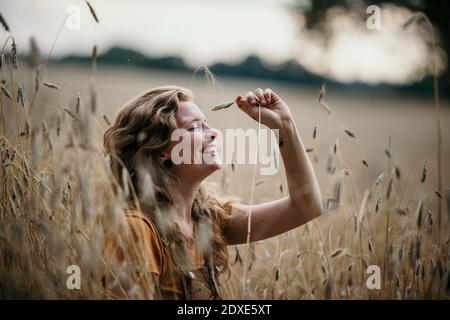 Happy woman sitting with eyes closed in agricultural field Stock Photo