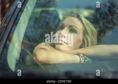 Thoughtful woman with arms crossed leaning inside car on windshield Stock Photo