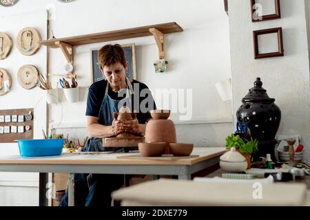 Mature female artist making pottery from brown clay in ceramic store Stock Photo