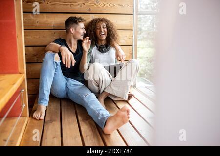 Cheerful young couple with digital tablet sitting on floor at home Stock Photo