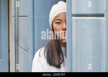 Young woman hiding behind wall while standing outdoors Stock Photo