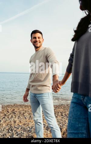 Smiling man holding woman's hand while standing at beach