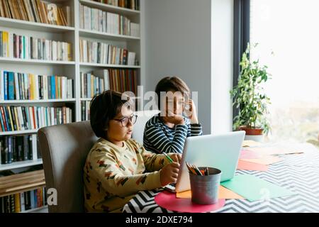 Boys e-learning through laptop while sitting in living room Stock Photo